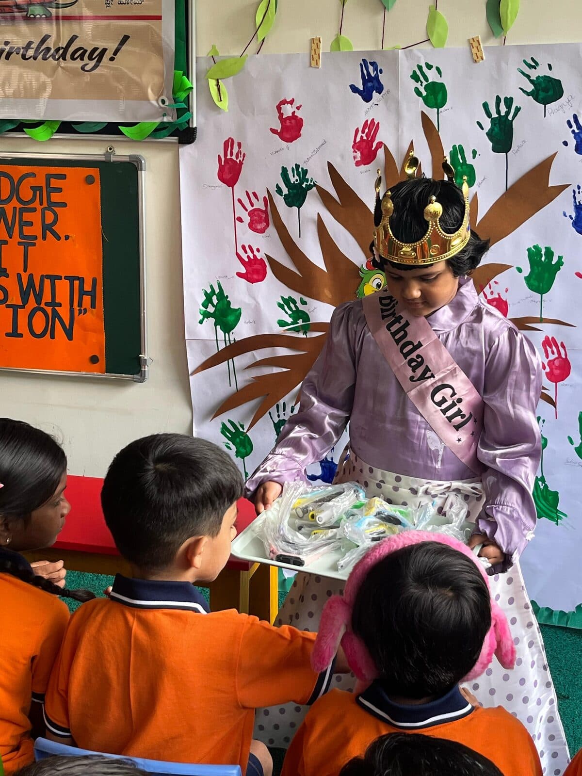 The birthday girl in a crown and sash sharing return gifts with friends at Turtles Play Home