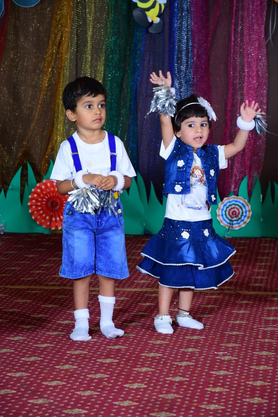 Two young children performing a pom-pom dance on stage at the Turtles Play Home Annual Day