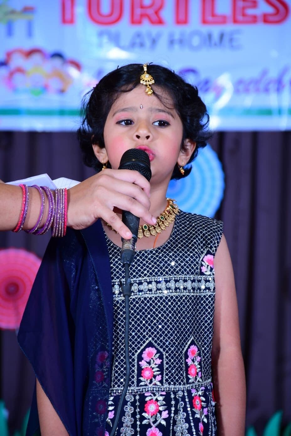 A young Turtles Play Home performer singing on stage at the Annual Day celebration